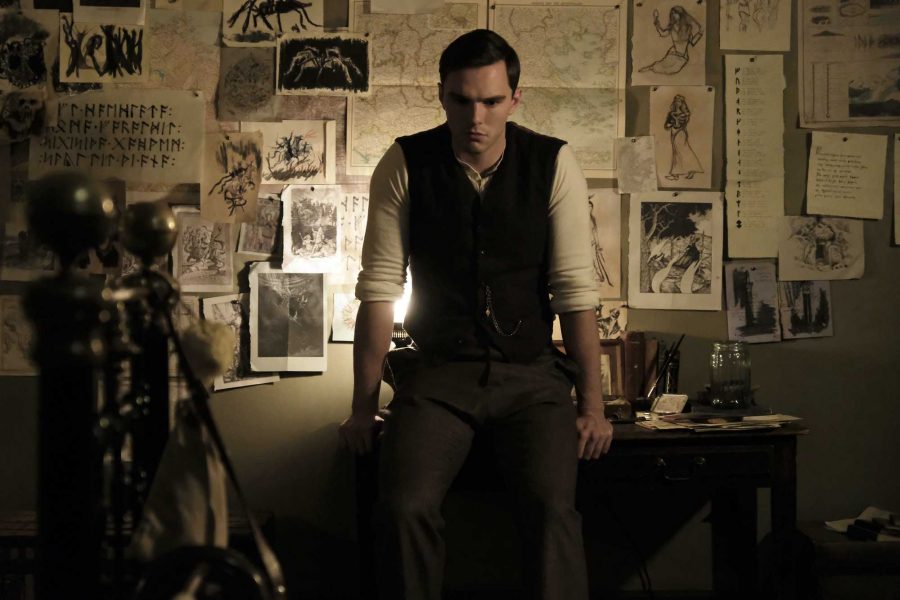 Nicholas Hoult as Tolkein in film, Tolkien, sitting on desk forward of his collection of artwork and writings. 