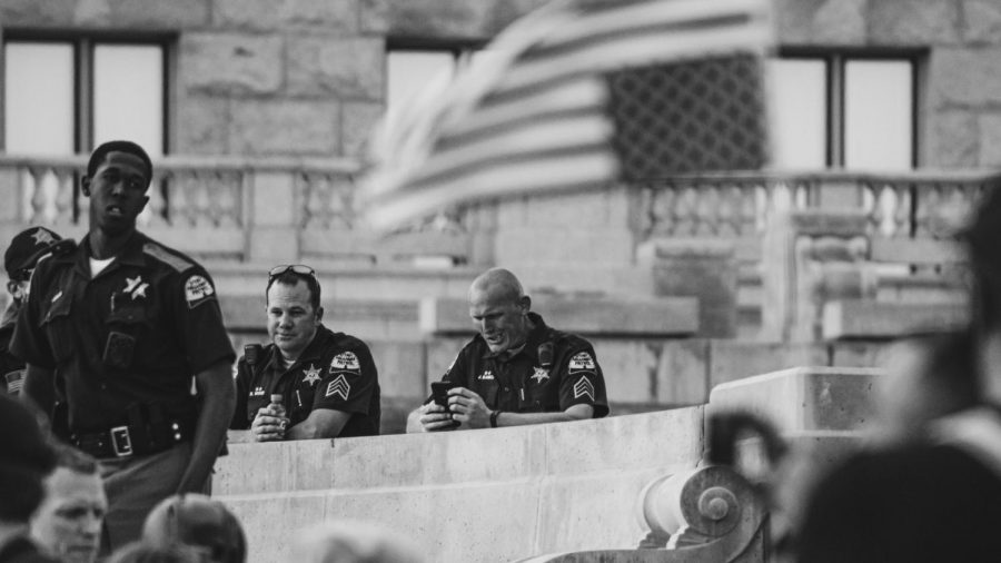 Utah Highway Patrol K-9 officer J. Banks (right) uses his phone as officers I. Lofton (far left) and B. Wood (center) look out over the crowd gathered to protest police brutality and corruption in front of the Utah State Capitol Building on June 4, 2020 (Photo by Mark Draper | Daily Utah Chronicle) 