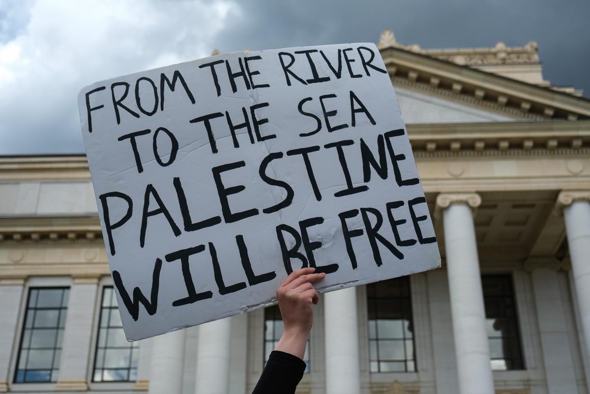 A pro-Palestine demonstrator holds up a sign in front of the John R. Park Building at the University of Utah during the Emergency Rally For Palestine on Monday, April 29, 2024. (Photo by Marco Lozzi | The Daily Utah Chronicle)